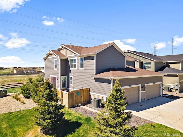 view of front facade featuring fence, concrete driveway, roof with shingles, cooling unit, and an attached garage