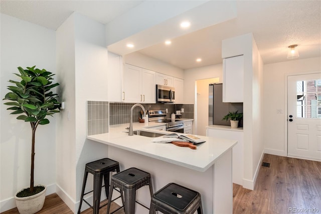 kitchen featuring a breakfast bar, kitchen peninsula, light hardwood / wood-style flooring, appliances with stainless steel finishes, and white cabinetry