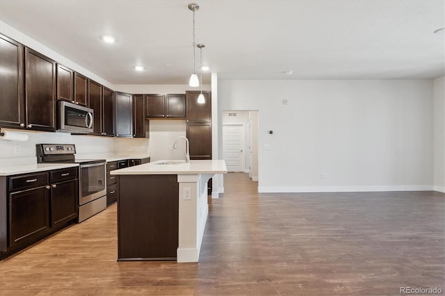 kitchen featuring dark brown cabinetry, decorative light fixtures, stainless steel appliances, an island with sink, and sink