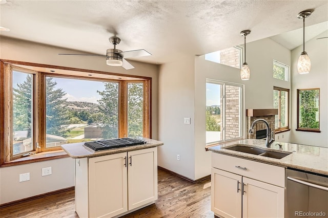 kitchen with stainless steel dishwasher, a kitchen island, sink, decorative light fixtures, and white cabinetry