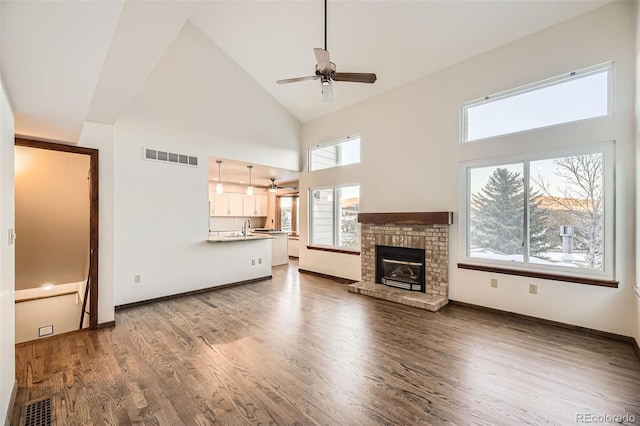 unfurnished living room with hardwood / wood-style floors, high vaulted ceiling, a healthy amount of sunlight, and a brick fireplace