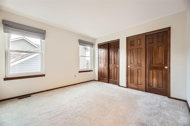 unfurnished bedroom with two closets and light colored carpet