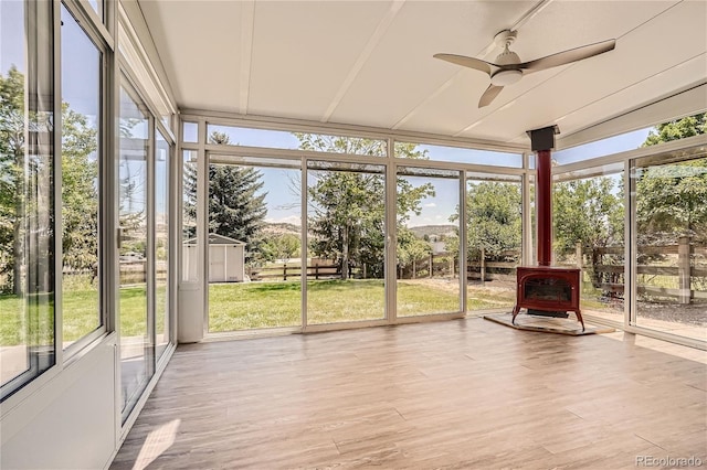 unfurnished sunroom with ceiling fan and a wood stove