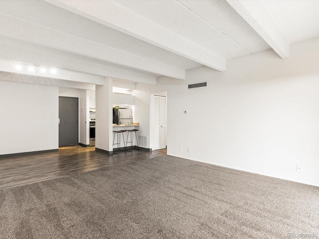 unfurnished living room with dark hardwood / wood-style floors, beam ceiling, and a textured ceiling