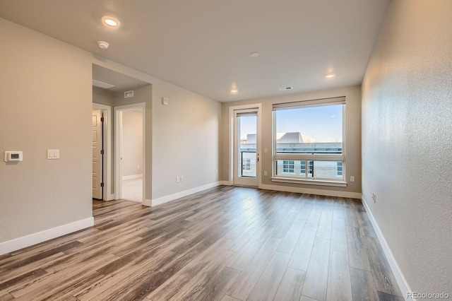 empty room with wood finished floors, baseboards, a textured wall, a smoke detector, and recessed lighting