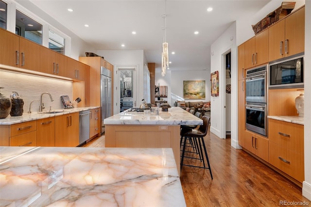 kitchen featuring hardwood / wood-style floors, decorative light fixtures, sink, a kitchen bar, and built in appliances