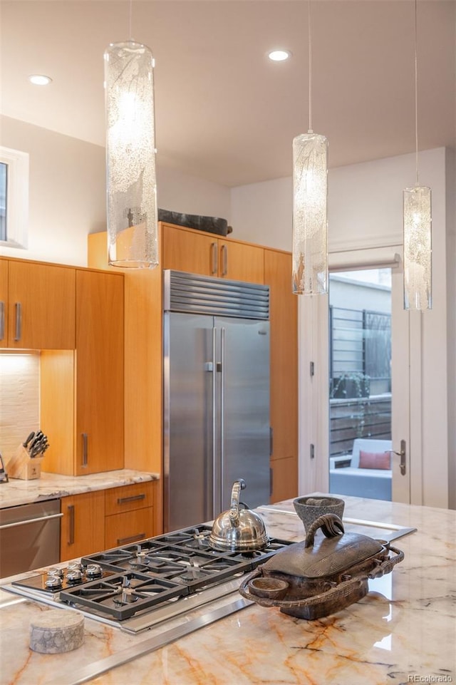 kitchen with pendant lighting, light stone counters, and stainless steel appliances