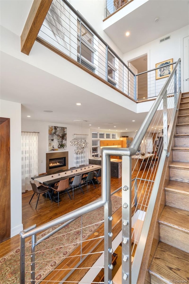 stairway with hardwood / wood-style floors, a towering ceiling, and beamed ceiling