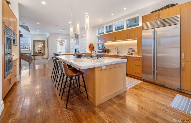 kitchen featuring appliances with stainless steel finishes, backsplash, hanging light fixtures, a center island, and light hardwood / wood-style floors