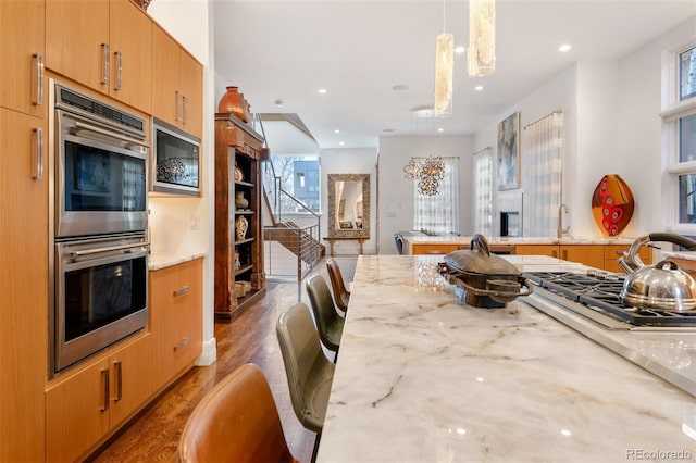 kitchen with a breakfast bar, light stone counters, hanging light fixtures, light wood-type flooring, and double oven