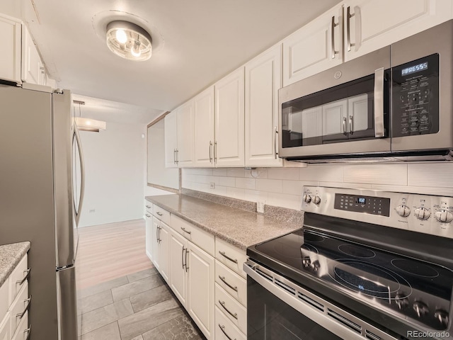 kitchen featuring appliances with stainless steel finishes, white cabinetry, light stone counters, and tasteful backsplash