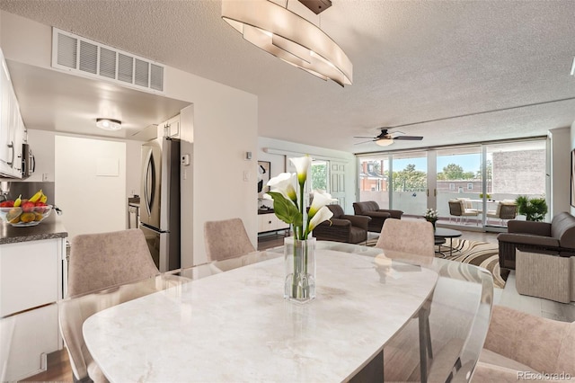 dining area with a ceiling fan, visible vents, a textured ceiling, and a wall of windows