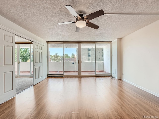 unfurnished room with expansive windows, a textured ceiling, light wood-type flooring, and baseboards