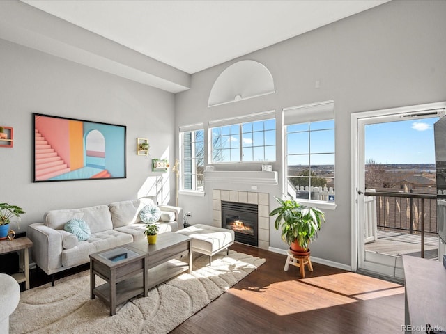 living room with a tiled fireplace, plenty of natural light, and wood finished floors