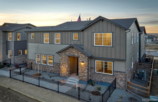 view of front of property with board and batten siding, central AC, fence, and a patio