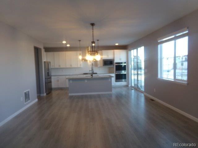 kitchen with pendant lighting, white cabinets, dark hardwood / wood-style flooring, stainless steel appliances, and a center island with sink