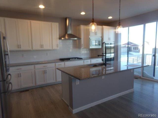 kitchen with white cabinetry, decorative light fixtures, stainless steel appliances, and wall chimney exhaust hood