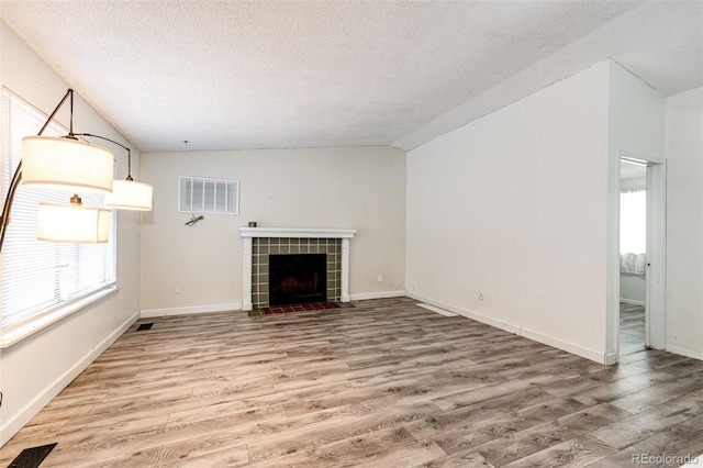 unfurnished living room featuring visible vents, vaulted ceiling, light wood finished floors, and a tiled fireplace