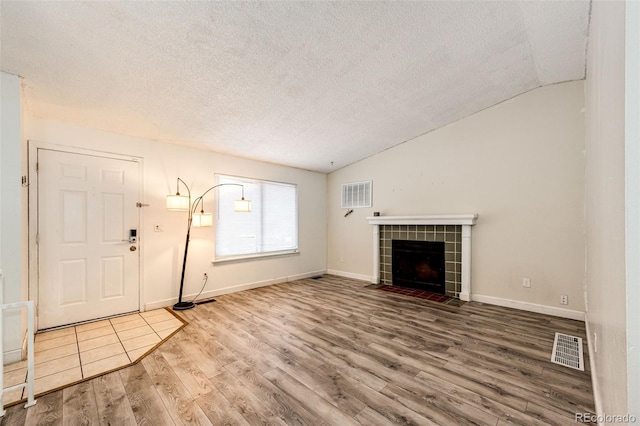 unfurnished living room with lofted ceiling, visible vents, a tile fireplace, and wood finished floors