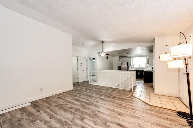 unfurnished living room with lofted ceiling, light wood-style floors, a ceiling fan, and a textured ceiling