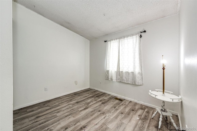 empty room featuring baseboards, a textured ceiling, visible vents, and wood finished floors