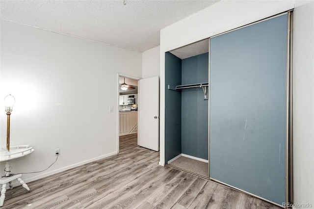 unfurnished bedroom featuring a textured ceiling, a closet, baseboards, and wood finished floors