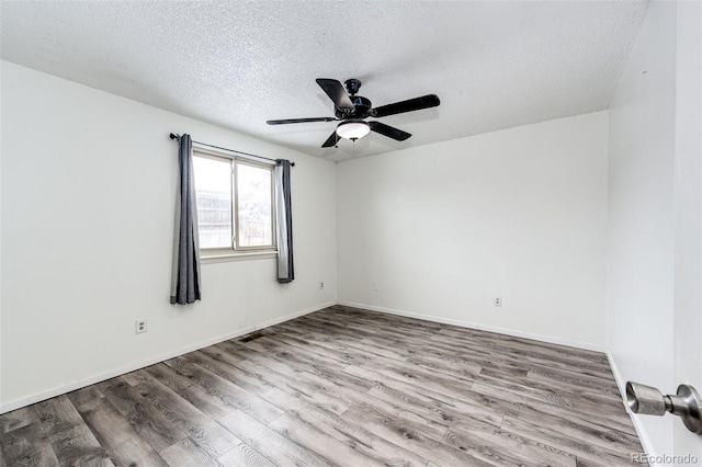 unfurnished room with ceiling fan, a textured ceiling, baseboards, and wood finished floors