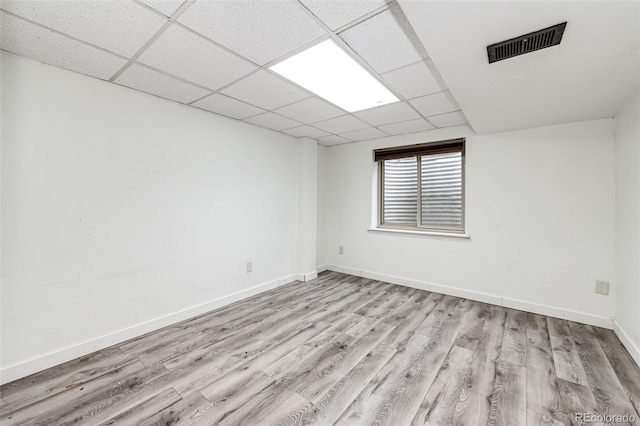 spare room with light wood finished floors, a drop ceiling, visible vents, and baseboards