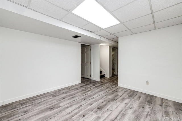 finished below grade area with a paneled ceiling, visible vents, wood finished floors, baseboards, and stairs