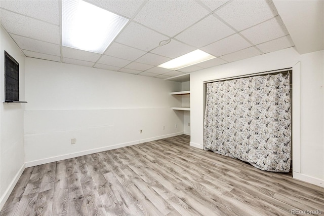 finished basement featuring a paneled ceiling, baseboards, and wood finished floors