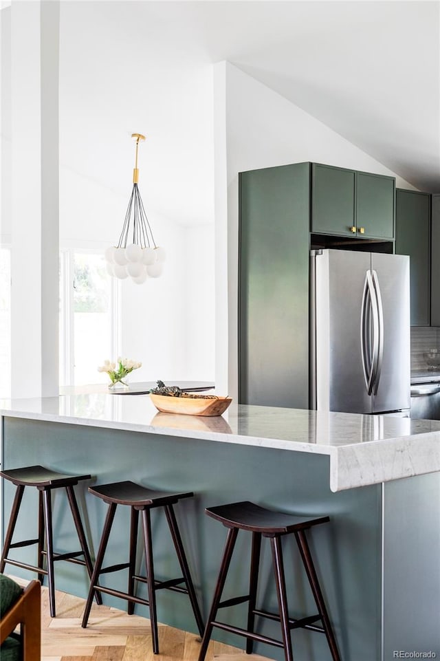 kitchen with green cabinetry, stainless steel refrigerator, a kitchen breakfast bar, and decorative backsplash