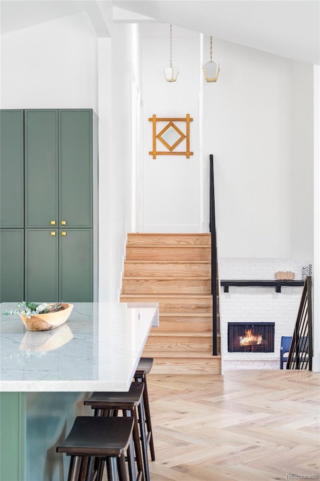 kitchen with hanging light fixtures, vaulted ceiling, a brick fireplace, green cabinetry, and a kitchen bar