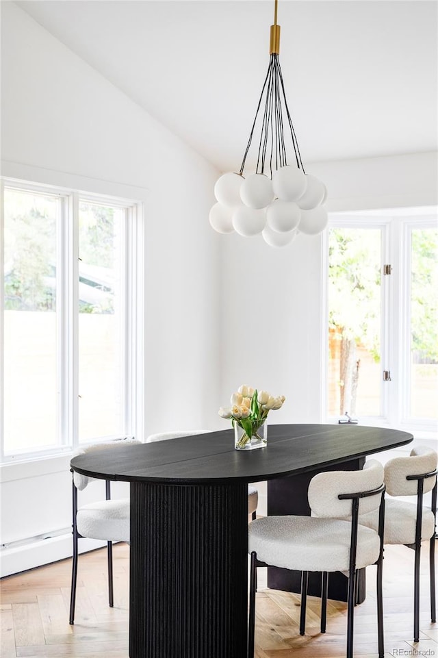 dining space featuring a notable chandelier, light hardwood / wood-style floors, vaulted ceiling, and plenty of natural light