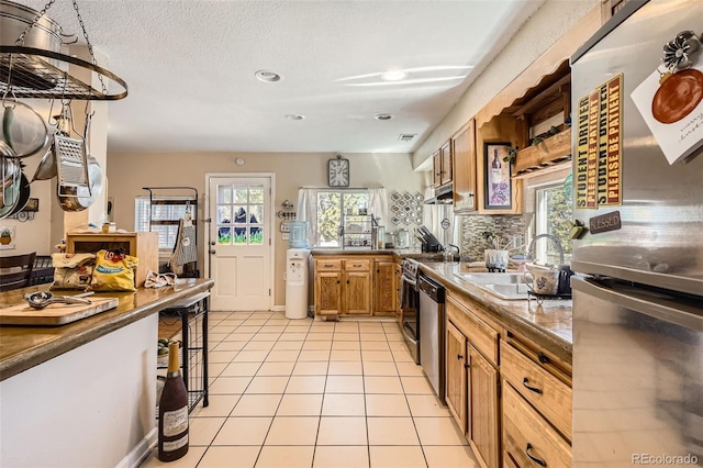 kitchen featuring freestanding refrigerator, a sink, brown cabinets, dishwasher, and light tile patterned floors