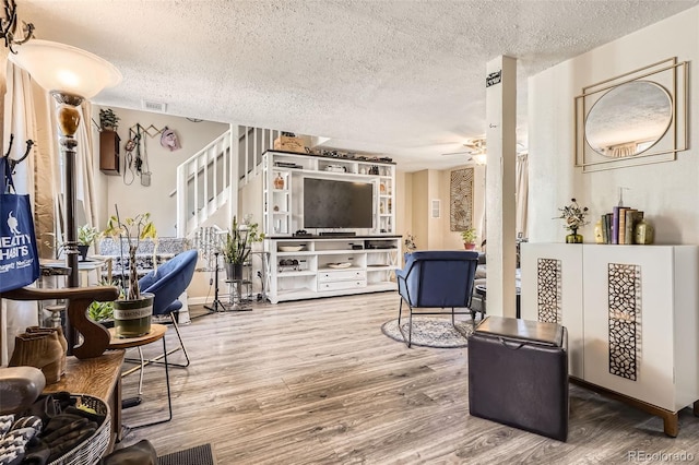 living area featuring a ceiling fan, a textured ceiling, visible vents, wood finished floors, and stairway