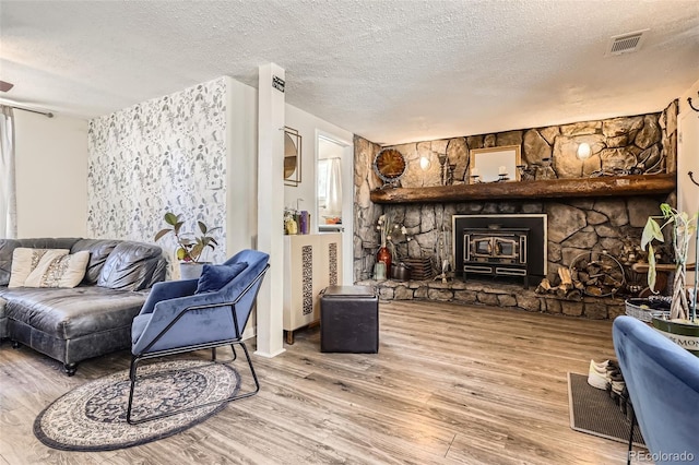 living room featuring a textured ceiling, wood finished floors, and a stone fireplace