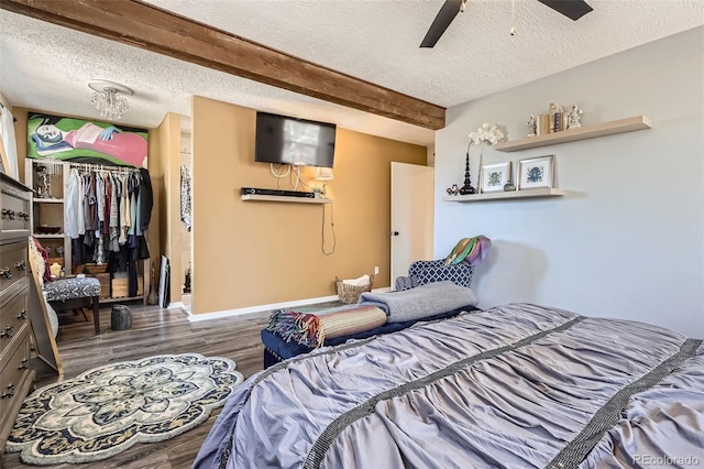 bedroom with a closet, a textured ceiling, ceiling fan, wood finished floors, and beam ceiling