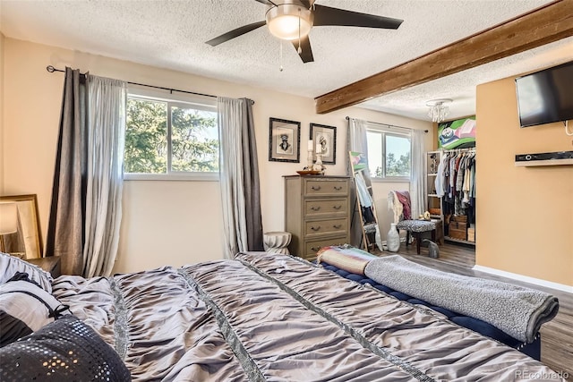 bedroom with a textured ceiling, wood finished floors, baseboards, and beamed ceiling