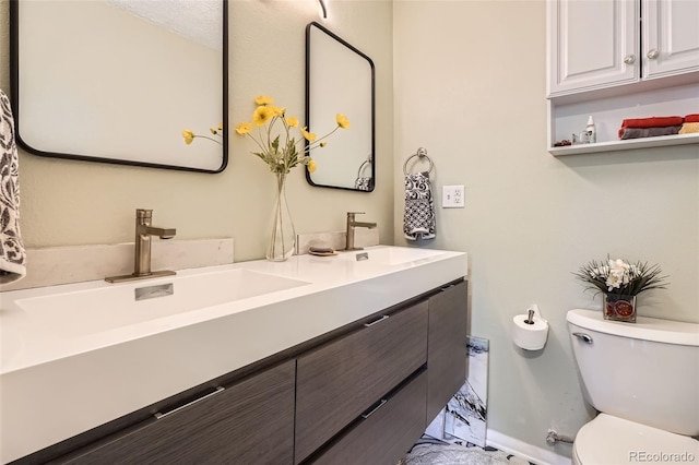 bathroom featuring toilet, baseboards, double vanity, and a sink