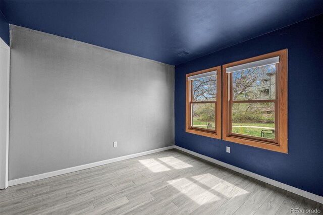 unfurnished room featuring baseboards, visible vents, and wood finished floors
