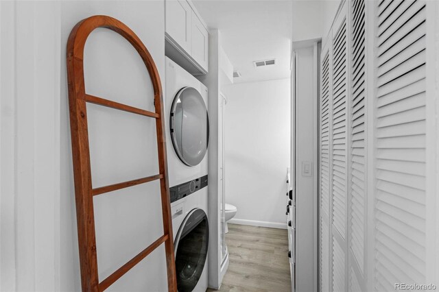laundry room featuring stacked washer and dryer, laundry area, light wood-style flooring, baseboards, and visible vents