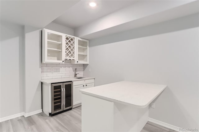 bar with backsplash, white cabinets, sink, light hardwood / wood-style flooring, and beverage cooler