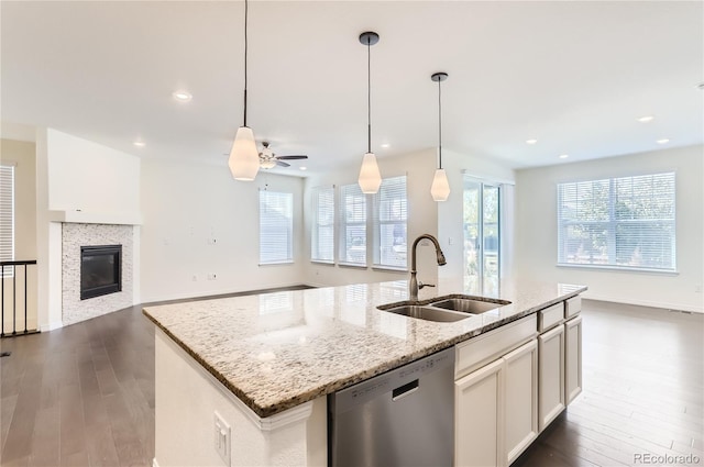 kitchen featuring dishwasher, sink, light stone counters, dark hardwood / wood-style floors, and an island with sink