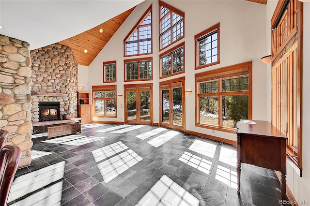 unfurnished living room featuring high vaulted ceiling, a stone fireplace, plenty of natural light, and baseboards