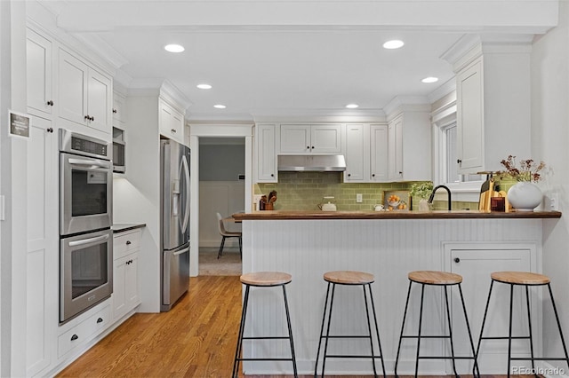 8132 Lodgepole Trl, Lone Tree, CO 80124 - kitchen with appliances with stainless steel finishes, under cabinet range hood, a peninsula, light wood-style flooring, and white cabinets