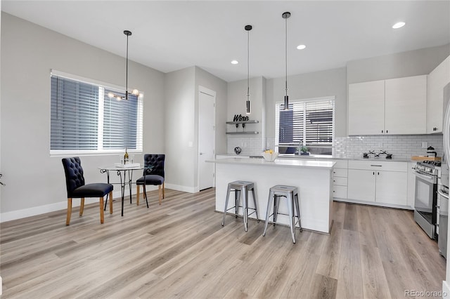 kitchen featuring sink, stainless steel gas range, white cabinets, decorative light fixtures, and a kitchen island