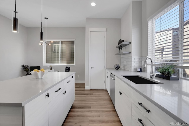 kitchen featuring sink, stainless steel dishwasher, decorative light fixtures, a kitchen island, and white cabinetry