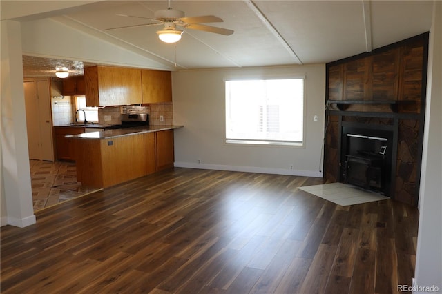 kitchen featuring vaulted ceiling, backsplash, kitchen peninsula, ceiling fan, and dark hardwood / wood-style floors