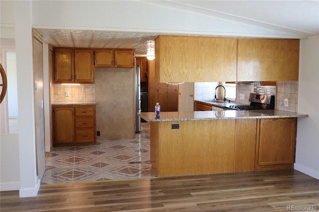 215 7th Ave, Deer Trail, CO 80105 - kitchen featuring stove, decorative backsplash, brown cabinetry, a peninsula, and lofted ceiling