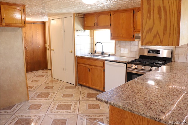 kitchen featuring light stone counters, sink, decorative backsplash, gas range, and white dishwasher